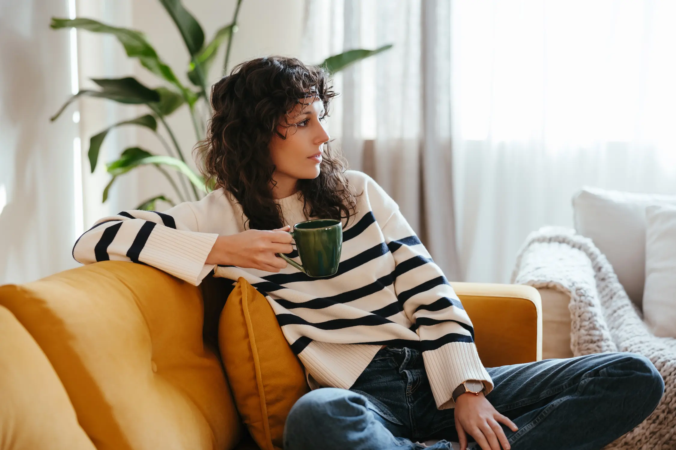 Woman holding coffee cup sitting on yellow couch